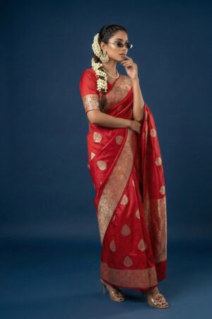 A rich ruby red Banarasi silk saree featuring elegant gold buta motifs and a broad golden border.